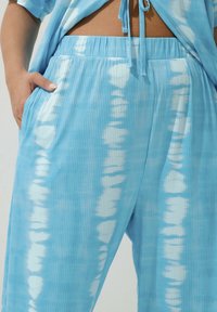 Ljusblå räfflade byxor med ett vitt tie-dye mönster och en elastisk midja med fickor. Tyget verkar mjukt och bekvämt.