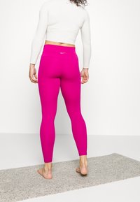 Růžové legíny s vysokým pasem a malým bílým logem na zadní straně. Hladký povrch, elastický materiál a délka ke kotníkům.
