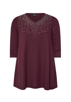 Blusa tunic burdeos con escote en V, mangas tres cuartos, y adornada con tachuelas plateadas alrededor del escote. Textura de tela suave.