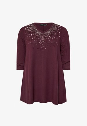 Bordeaux tunika med v-hals, trekvartærmer og udsmykket med sølvnitter rundt om halsudskæringen. Glat stoftekstur.