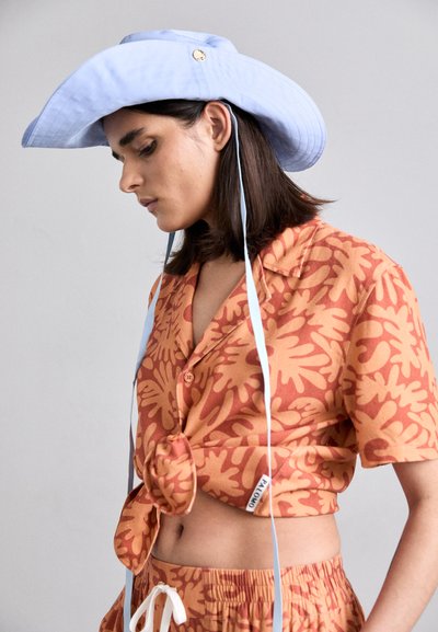 Short-sleeve shirt with orange and tan leaf patterns, tied at the waist. Light blue wide-brim hat with adjustable ties, gold accent.
