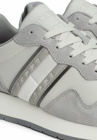 Zapatillas deportivas grises que combinan texturas de cuero liso y ante, con una suela blanca gruesa y detalles de marca en relieve.