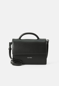 Sac en cuir noir à porter croisé avec une forme structurée, une poignée supérieure et une sangle réglable. Il est doté d'une fermeture à rabat magnétique et d'un détail de logo.