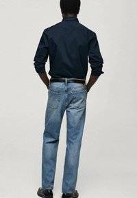 Marineblauw overhemd met lange mouwen in combinatie met lichtblauwe denim jeans; beide hebben een klassieke fit. De jeans hebben een vervaagde textuur en achterzakken.