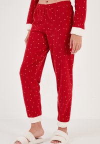 Röda pyjamasbyxor med vita stjärnmönster, vertikala ränder och mjuka, plyschiga vita manschetter. Tillverkade av ett bekvämt, strukturerat tyg.