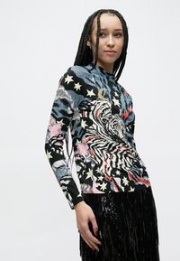Top de manga larga con base negra y un vibrante estampado de tigre, estrellas y patrones abstractos, confeccionado en un material suave y elástico.