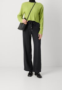 Grön kabelstickad cropped tröja, svarta vida byxor och svarta skor. Liten svart crossbody-väska. Släta texturer och avslappnad passform.