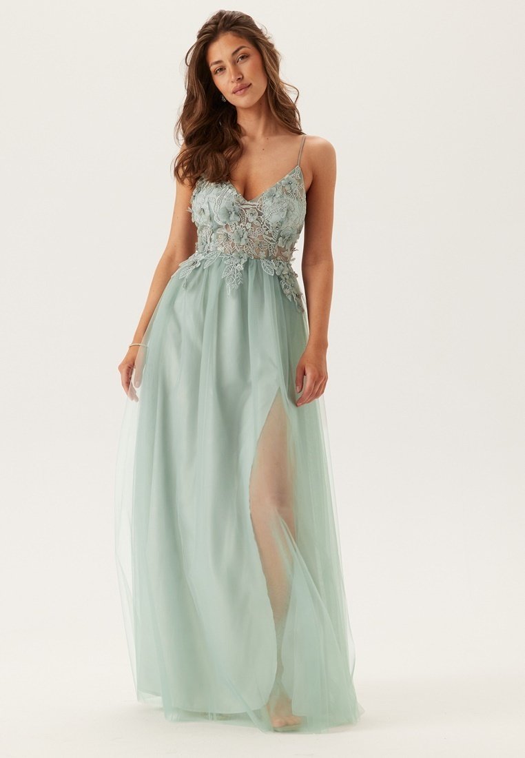 Abito da sera in un teal chiaro con scollatura profonda, corpetto in pizzo floreale e gonna trasparente con uno spacco alto fino alla coscia. Spalline a spaghetto.