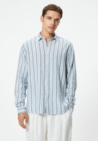 Camisa de manga larga con botones que presenta rayas verticales en azul y blanco, confeccionada en una tela ligera con cuello y un corte clásico.