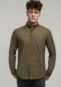 Oliwkowa koszula na guziki z kieszonką na piersi, długimi rękawami i miękką fakturą. Posiada małe logo na kieszeni.