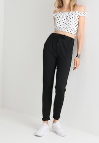 Pantaloni neri taper con vita regolabile, abbinati a una maglietta bianca off-shoulder con pois neri. Indossati con sneakers bianche.