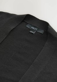 Cardigan nero a maglia con scollatura a V. Tessuto morbido, cuciture minime e un'etichetta con scritto "NEXT" cucita al collo.