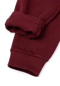 Burgunderfarbene Sweatpants mit Umschlägen, die einen umgeschlagenen Saum zeigen und den weichen, strukturierten Innenstoff vor einem weißen Hintergrund zur Schau stellen.