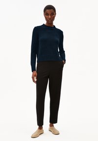 Dunkelblauer gerippter Strickpullover mit Rundhalsausschnitt, kombiniert mit schwarzen schmal zulaufenden Hosen und beigen Slippern. Einfaches, strukturiertes Design.