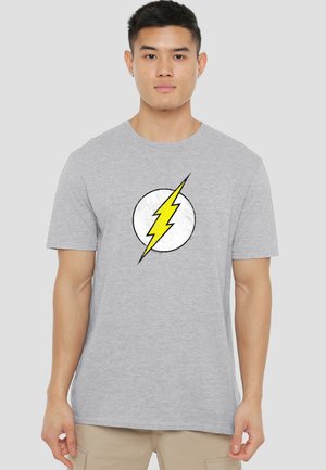 Young man wearing a gray t-shirt with a yellow lightning bolt inside a white circle on the front, standing against a plain background.