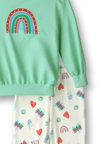Mintgroene sweatshirt met geribde boorden en een regenbooggrafiek. Crème broek met een patroon van vlinders, harten en lachende gezichten.