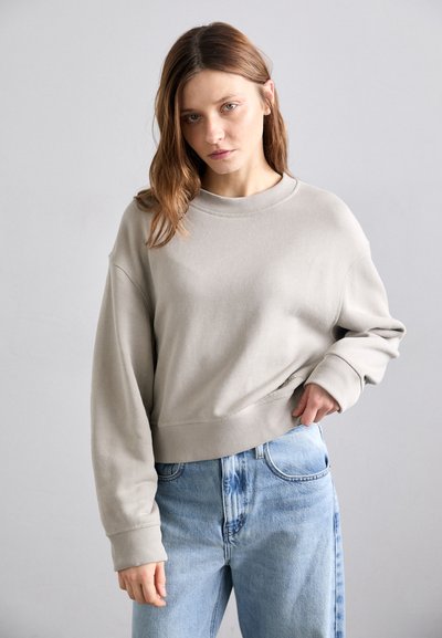 Lys grå cropped sweatshirt med en bred halsudskæring og ribbede manchetter, parret med lyseblå højtaljede jeans, der har en afslappet pasform.