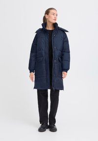 Námořnický puffer kabát s oversized střihem, předními kapsami, vysokým límcem a detaily se stahovací šňůrkou; hladká textura a zipy pro zapínání.