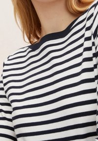 Top a righe blu navy e bianche in maglia con scollo rotondo. Il tessuto sembra morbido con una superficie liscia e strisce orizzontali uniformi.
