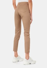 Hnědé slim-fit kalhoty s středně vysokým pasem, zúženými nohavicemi a dvěma zadními kapsami, doplněné bílými teniskami. Hladká textilie.