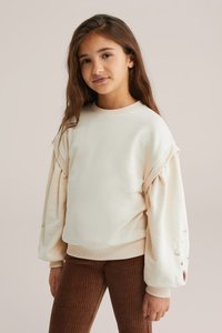 Pullover in crema con maniche larghe, polsini a costine e orlo arrotondato. Presenta dettagli ricamati di stelle e lune sulle maniche.