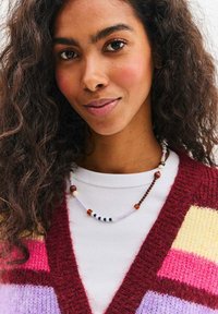 Kolorowy dziany kardigan z głębokim dekoltem w kształcie litery V, ozdobiony paskami w kolorach fioletowym, różowym i żółtym. Naszyjnik z koralików o różnych kolorach.