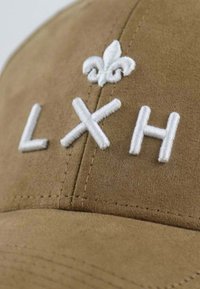 Braune Wildlederkappe mit weißen gestickten Buchstaben "LXH" und einem Lilien-Symbol. Verfügt über sichtbare Nähte und eine glatte Textur.
