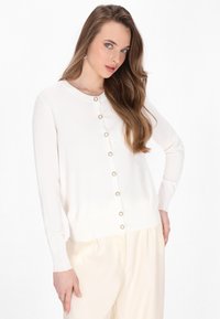 Cardigan bianco lavorato a maglia con scollatura rotonda, caratterizzato da otto bottoni decorativi sul davanti. Maniche lunghe con polsini e orlo a costine.
