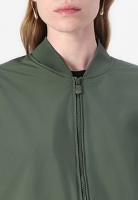 Groene bomberjack met een ritssluiting, geribbelde kraag en textielstof. Het ontwerp heeft een soepele afwerking en strakke lijnen.