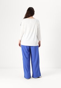 Wit langetermijnshirt en losvallende blauwe broek met een gladde textuur, voorzien van een ontspannen ontwerp en een ronde halslijn aan de achterkant.