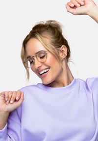 Cirkulære metalbriller med tynde rammer, lyse lilla sweatshirt, glat stof, lys hudtone, smilende udtryk, hænderne løftet.