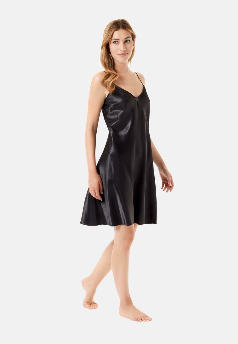 Vestido de satén negro tipo slip con escote en V y tirantes finos ajustables, que presenta un dobladillo de corte acampanado y una textura suave. Modelo descalzo.