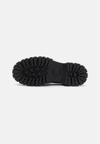 Black rubber sole with deep tread patterns, featuring pointed lugs for traction. Smooth texture with a circular logo near the center.