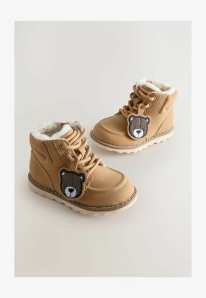 Smešane dječje čizmice u smešanoj boji s bež potplatima, toplom bijelom krznu unutrašnjosti, vezanjem sprijeda i aplikacijama lica mede pričvršćenim na vezicama.