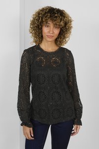 Top in pizzo nero a maniche lunghe con motivi floreali intricati, scollo a forma di scallop e polsini aderenti. Abbinato a jeans di denim scuri.