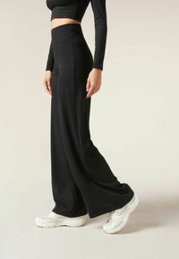 Black wide-leg athletic pants made from a smooth, stretchy fabric, featuring a high waistband and paired with white sneakers.