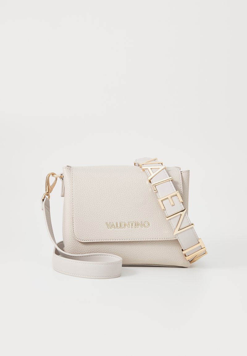 Béžová kožená crossbody taška s textúrovaným povrchom, preklápacím uzáverom, logom v zlatej farbe a nastaviteľným ramenným popruhom s písmenovými akcentmi.