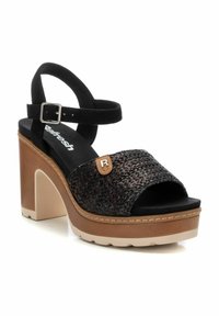 Sandali platform in suede nera con cinturini intrecciati marrone scuro, fibbia regolabile alla caviglia e tacco testurizzato color beige. Presentano un dettaglio del logo.