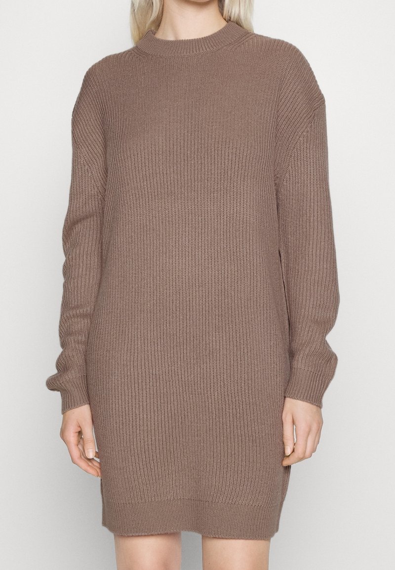 Femme portant une robe pull en maille côtelée à manches longues et longueur genou, couleur taupe marron.