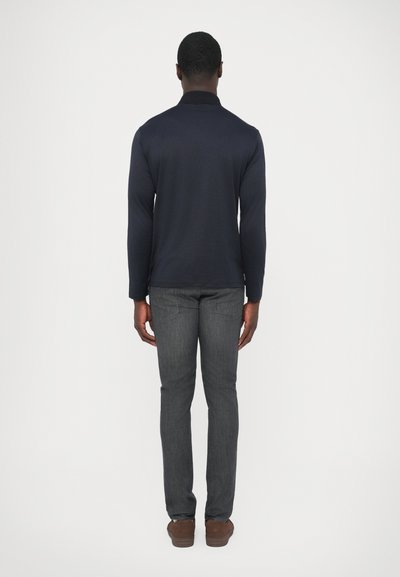 Tengerészkék hosszú ujjú galléros póló, szürke karcsúsított farmerrel párosítva. A ruházat sima textúrájú és minimális részletességű.