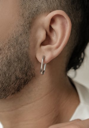 Silberne Creolen werden in einer Nahaufnahme eines Ohres präsentiert, mit einer glatten, polierten Oberfläche und einem kreisförmigen Design. Die Haare sind kurz geschnitten.