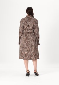 Smeđa haljina midi dužine s leopard printom, dugim rukavima, pojasom u struku i glatkim materijalom; nosi se uz crne sandale s visokom potpeticom i trakama.
