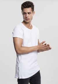 Fehér pamut póló rövid ujjakkal és ívelt aljjal, bal oldalon cipzár részlettel, fekete, slim fit farmernadrággal párosítva.