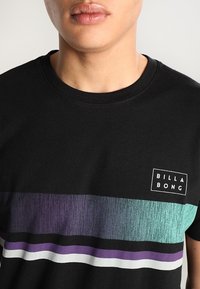 Svart bomullströja med rund hals som har horisontella ränder i turkos, lila och vitt, med en liten "BILLA BONG"-logotyp.