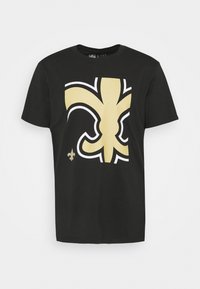 Černé bavlněné tričko s velkým zlatým a bílým grafickým vzorem fleur-de-lis na přední straně a menší verzí v dolním levém rohu.