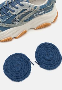 Denim sneaker featuring a distressed pattern in blue with a white sole and orange accents, paired with two textured navy blue shoelaces.