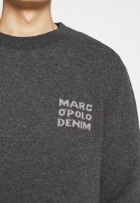 Dunkelgrauer Strickpullover mit einem runden Halsausschnitt und einem weißen Logo-Druck mit der Aufschrift "MARC O'POLO DENIM" auf der Vorderseite. Weiche Textur.