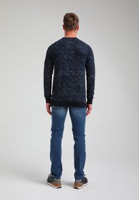 Camiseta de manga larga azul marino con un patrón texturizado y puños acanalados, combinada con jeans azules y zapatillas negras, vista desde la parte trasera.