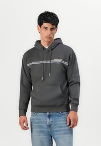 Hoodie gris en tissu doux, avec une poche avant, une capuche à cordon de serrage et un design à rayures horizontales sur la poitrine.