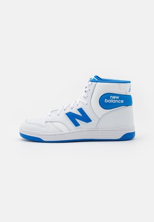 Baskets montantes blanches New Balance avec des accents bleus et logo, semelle plate et lacets à l’avant, vues de profil.